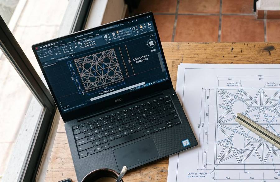 Laptop con una celosía de fachada abierta en CAD, junto al plano impreso del mismo detalle